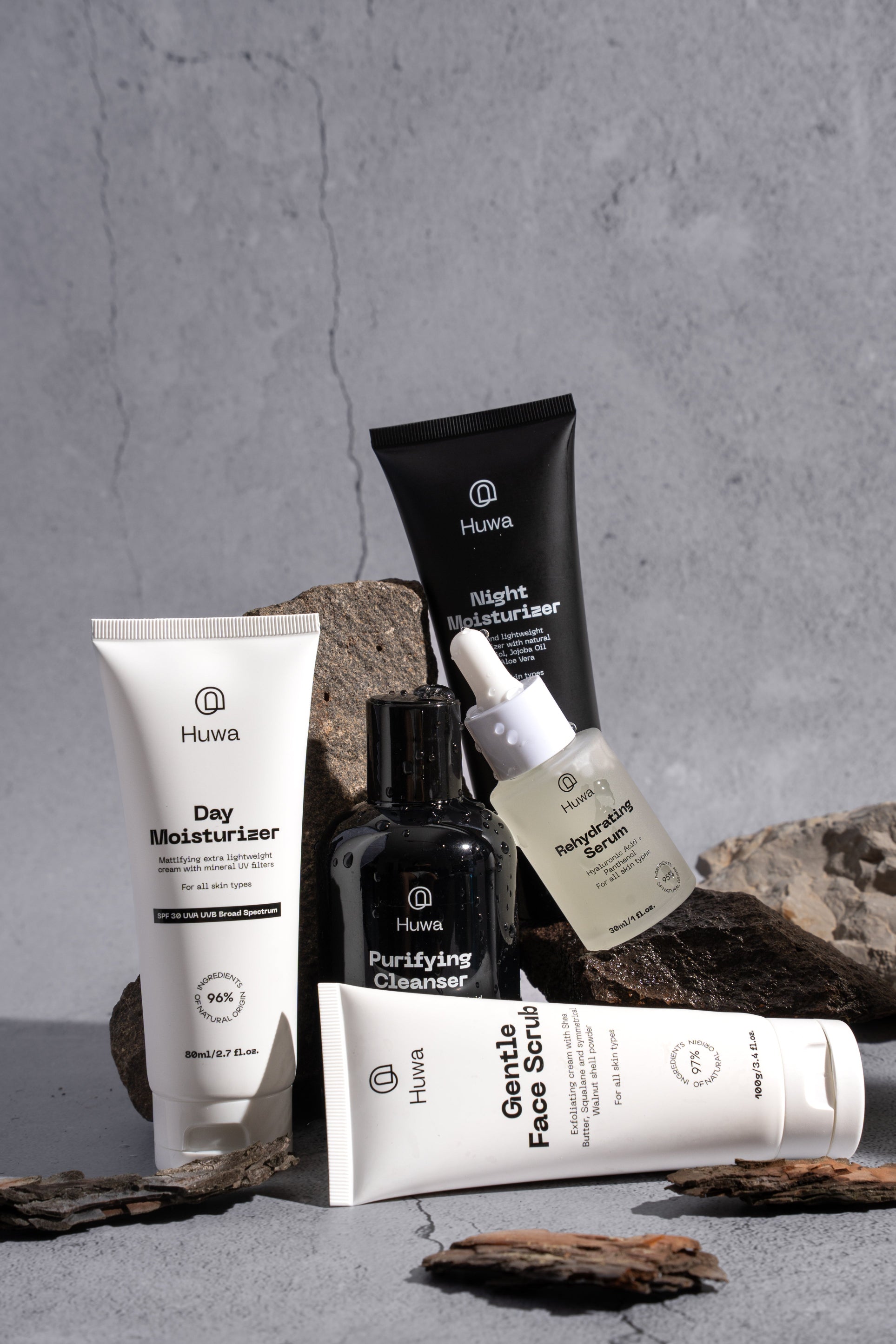 Huwa skincare product set misted on a textured surface with a gray stone background