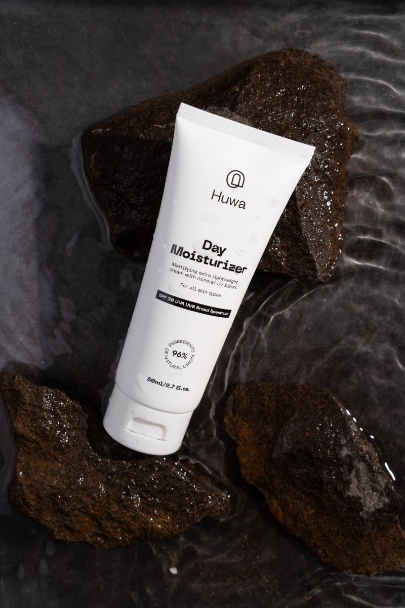 Huwa Day Moisturizer with SPF and mattiying cream tube on a dark stone background in water with small waves