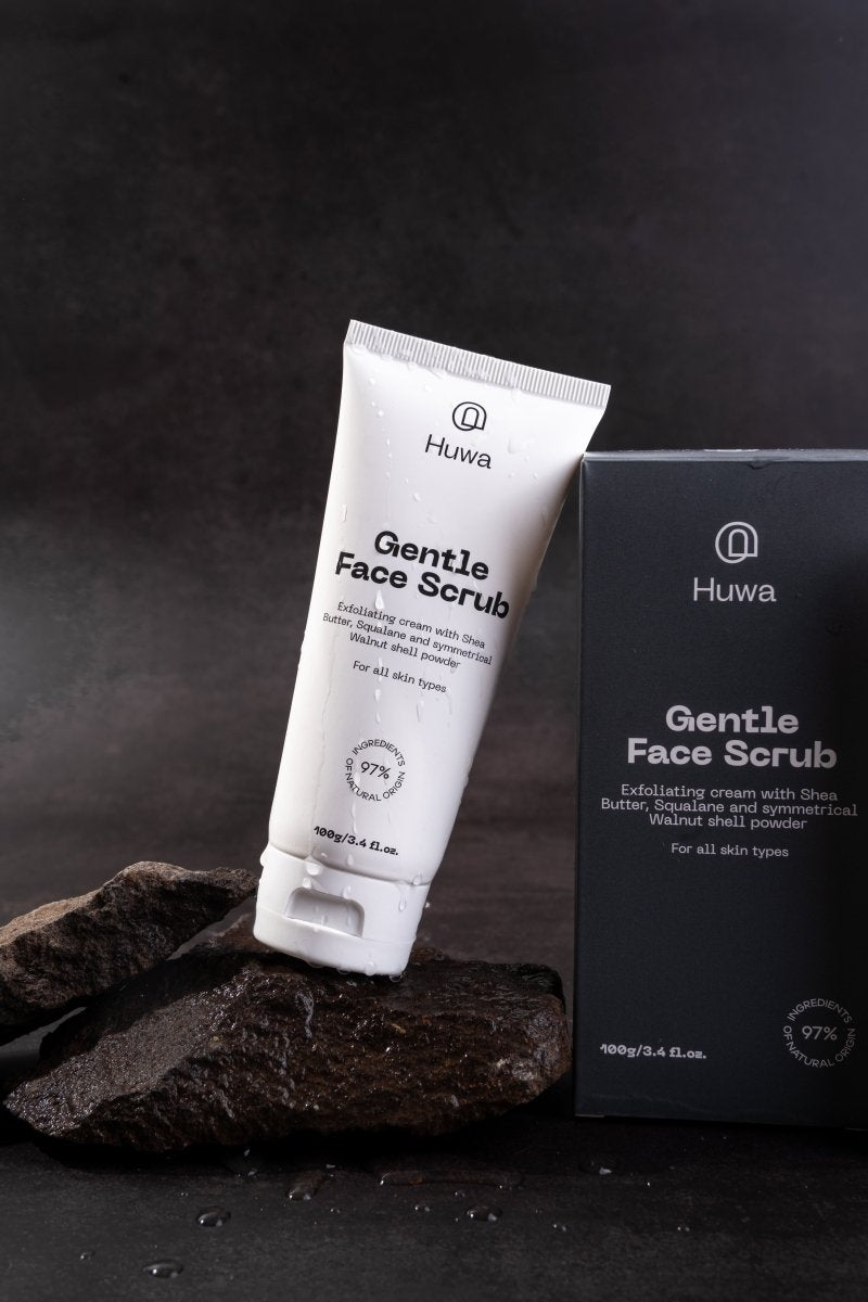 Huwa Gentle Face Scrub tube and packaging box on a dark background on a rock with drops of water on the tube