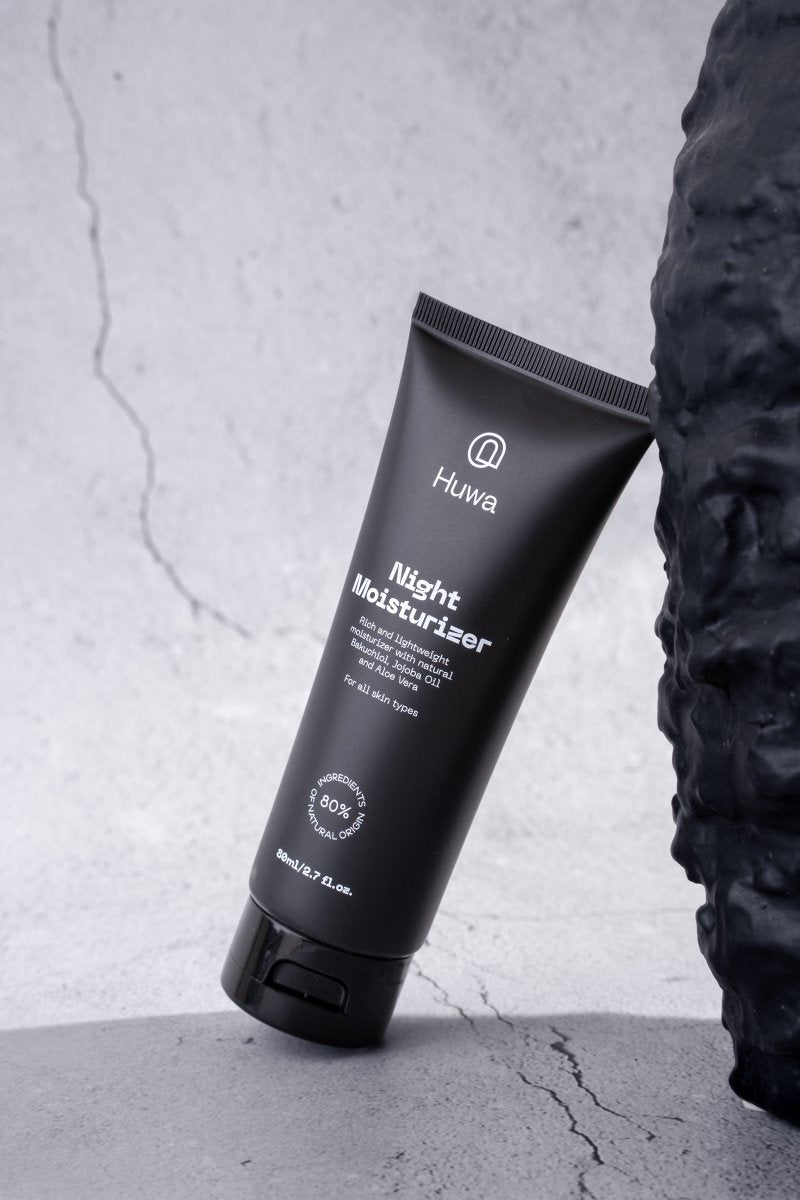 Black tube of Huwa Night Moisturizer on a black rock with a gray background leaning side and front view