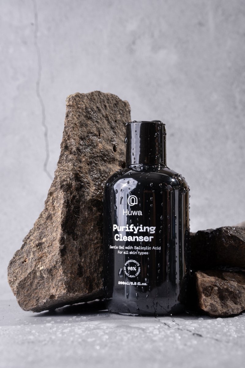 Black bottle of purifying cleanser from Huwa Skincare against a gray and brown stone misted with water 