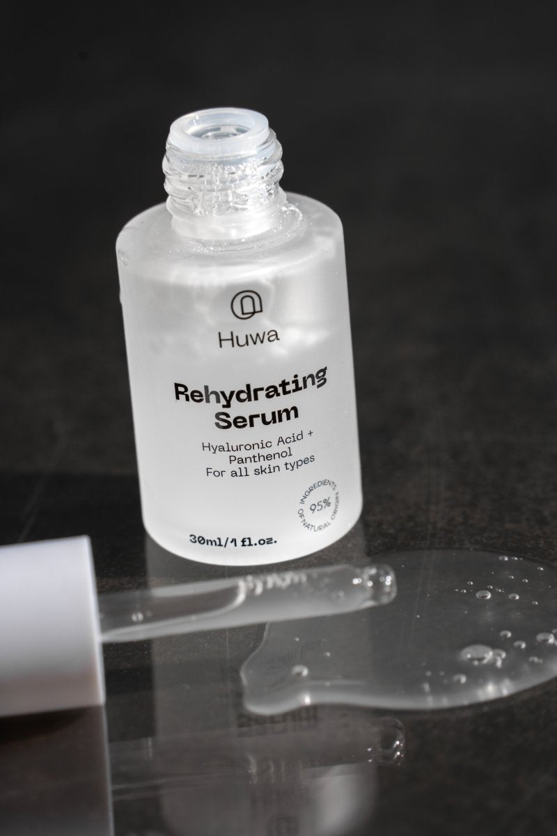 Huwa Skincare Rehydrating Serum bottle on a reflective surface with a dark background with dropper on the surface and hydrating serum on the surface with bubbles