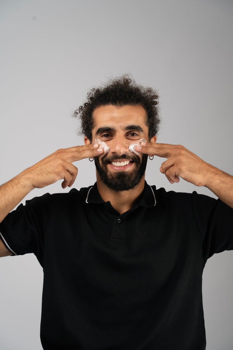 Man applying huwa skincare care gentle face scrub cream to his face with a neutral background the man is smiling and happy and his face is soft