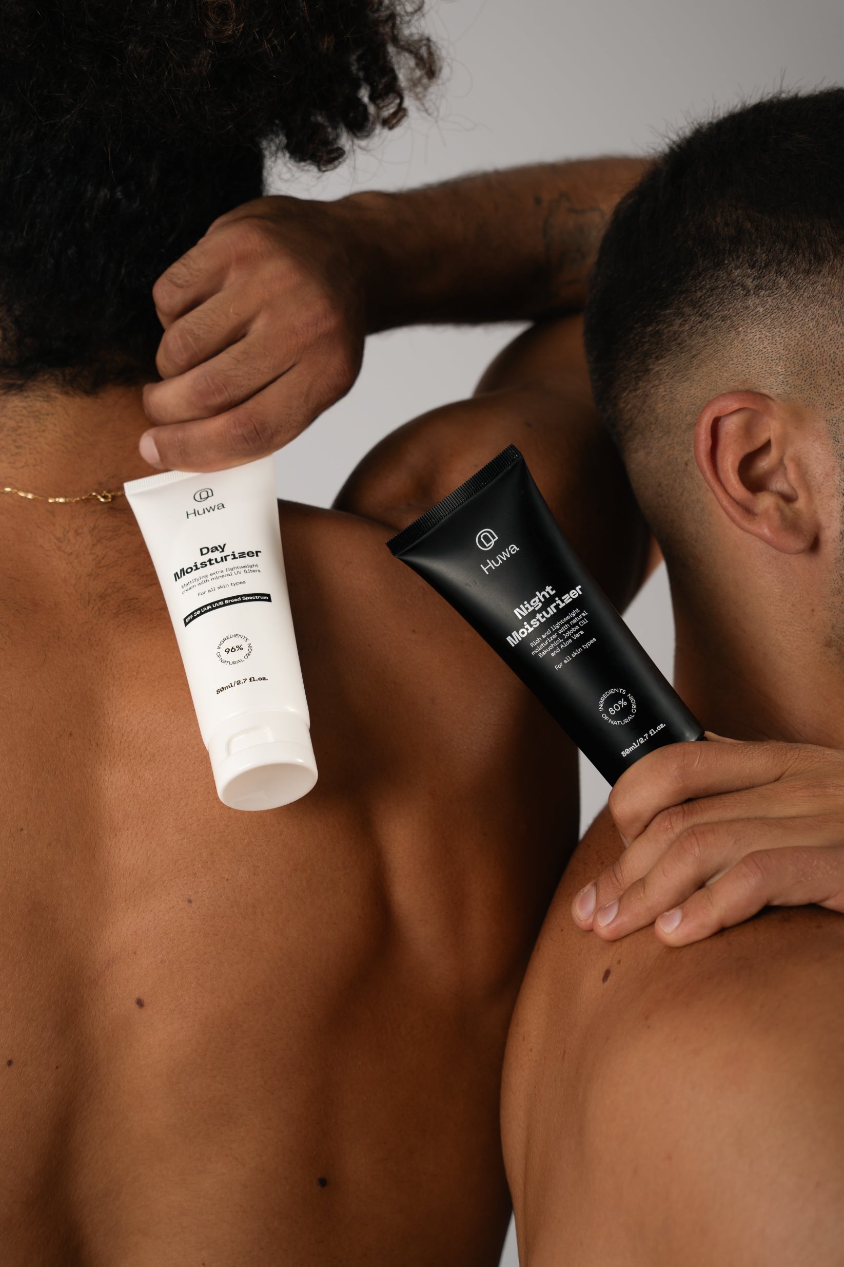 Two tubes of skincare product held by a person against their shoulders and back on a background