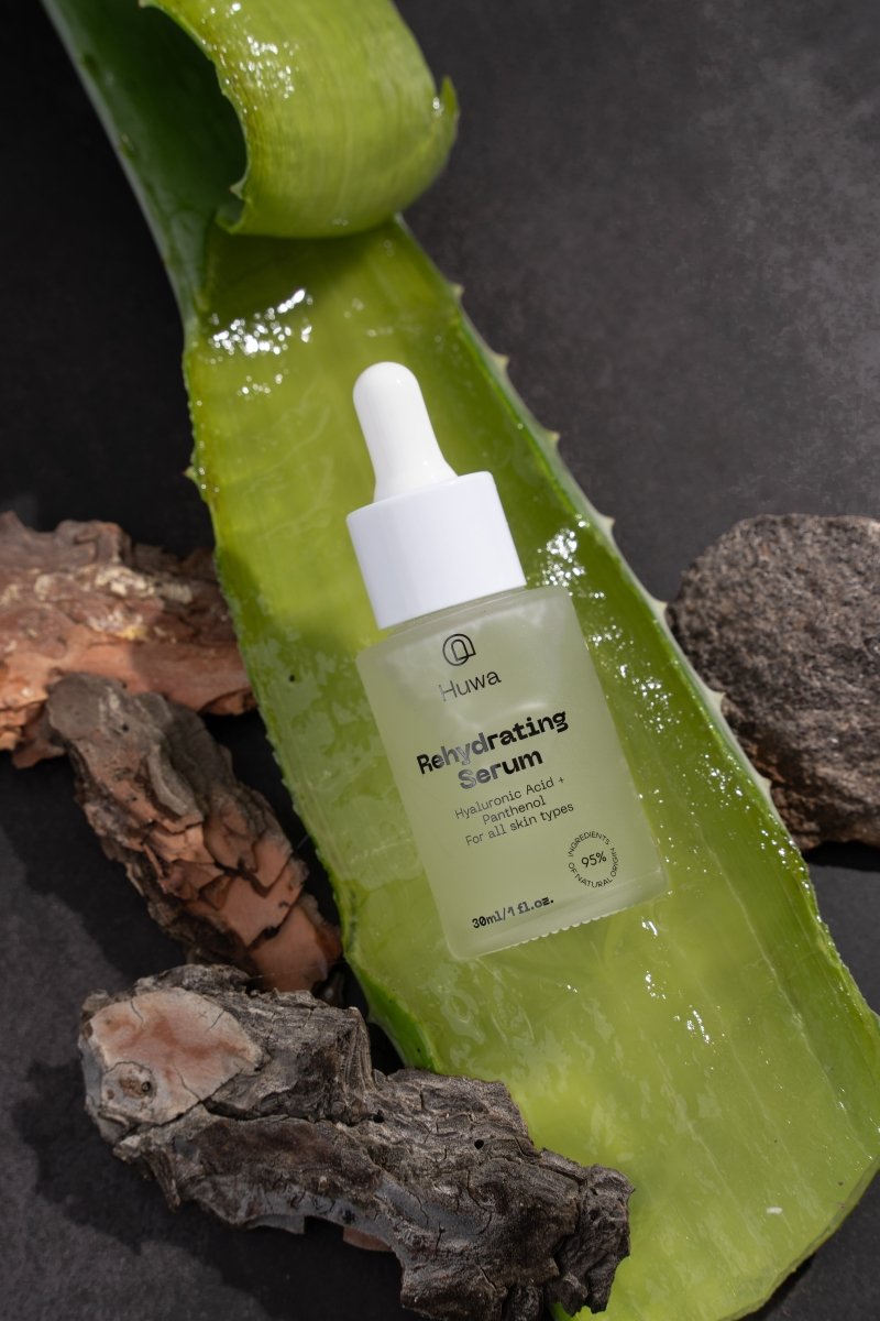 Huwa Skincare serum bottle which is frosted glass with white dropper on a natural background as the leaf of aloe vera